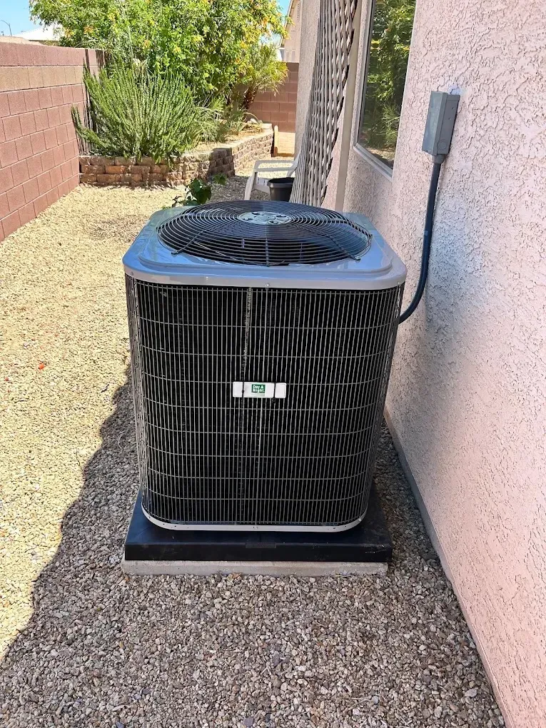 Outdoor air conditioning unit beside a house, surrounded by gravel and plants.
